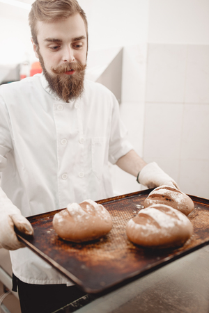 Charismatic baker holds the baking tray with newly-baked bread in the bakeryの写真素材