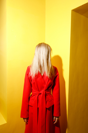 Fashion young girl blogger dressed in stylish red coat poses on the background of yellow walls in the show roomの写真素材