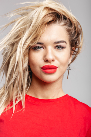 Young blond girl with a red  lipstick short  in a red t-shirt poses staying against a wall in the studioの写真素材