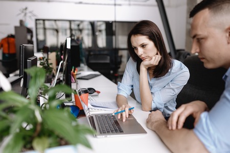 Beautiful woman and guy dressed in office style clothes are working together with laptop sitting at...