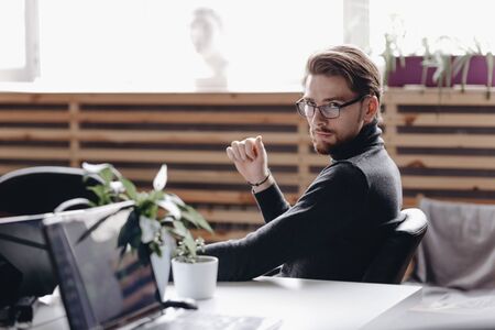 The guy dressed in casual office style clothes is sitting in an office chair at desk in the modern officeの写真素材