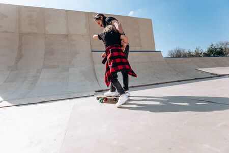 Father and his little son dressed in the casual clothes ride skateboards in a skate park with slides...