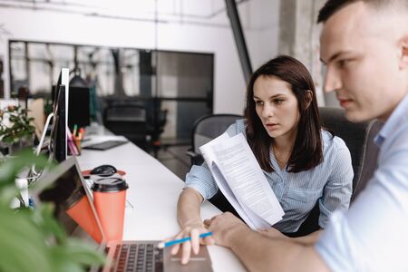 Beautiful woman and guy dressed in office style clothes are working with documents sitting at desks...