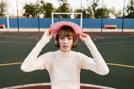 Stylish girl in a gently pink dress and pink visor is standing at the sports field on a summer sunny dayの写真素材