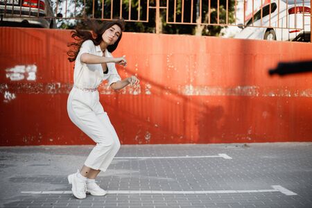 Young girl dressed in white shirt is dancing modern dance in the street against a painted concrete wall in the sunny dayの写真素材