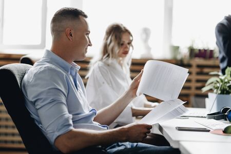 Beautiful woman and guy dressed in office style clothes are working sitting at desks in the light modern office equipped with modern office equipmentの写真素材