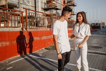Young stylish guy and girl are standing in the street on the background of urban building in the warm dayの写真素材