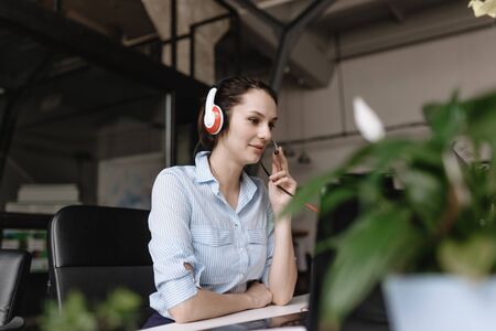 Young brunette woman dressed in office style clothes is talking to customers through the headset...