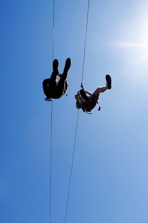 people zip lining through blue skyの写真素材