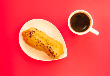 eclair and coffee on pink background.