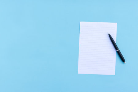Blank white paper and pen isolated on blue background. After some edits.の写真素材