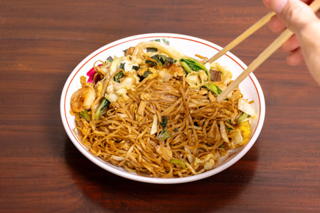 Fried noodle with chicken and vegetables in a white bowl on a wooden table. After edits.の写真素材