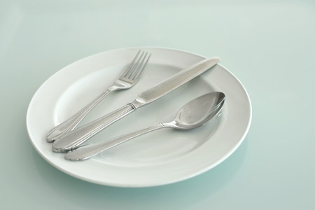 spoon fork and knife on empty white plateの写真素材