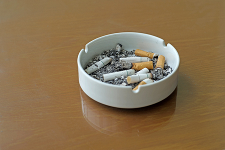 smoked cigarettes in white ashtray on wooden tableの写真素材