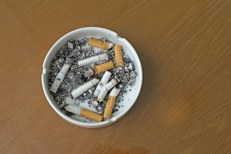 smoked cigarettes in white ashtray on wooden tableの写真素材