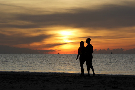 silhouette of couple walking on the beach with beautiful sunrise backgroundの写真素材