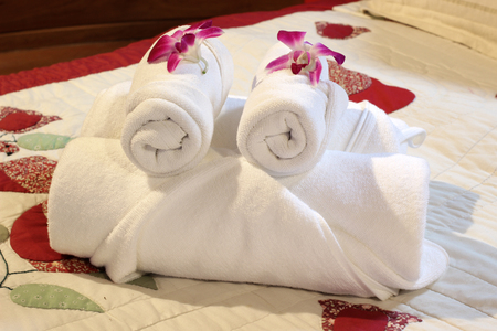 white bath towels rolled and piled on the bedの写真素材
