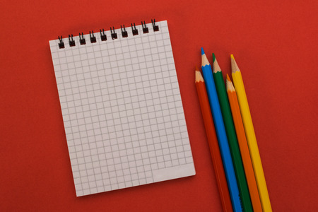 notebook and colored pencils on a red backgroundの写真素材