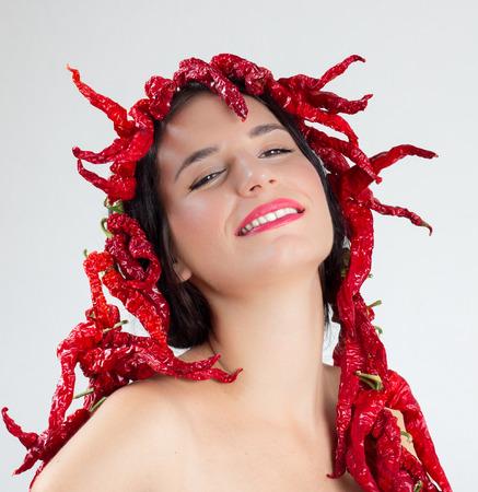 Portrait of a girl with red dry hot peppers around her head and bodyの写真素材