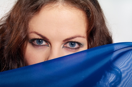 girl with blue eyes and brown curly hairs looks over blue scarf on white backgroundの写真素材