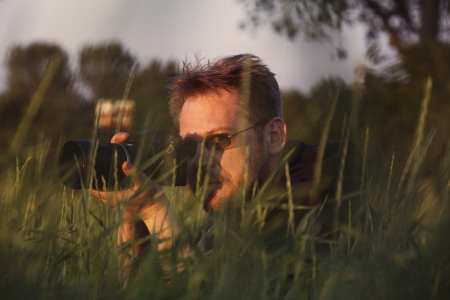 Photographer looks at camera taking picture while lying on grass in sunsetの写真素材