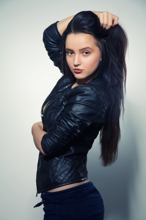 pretty brunette girl in leather jacket smiling at gray backgroundの写真素材