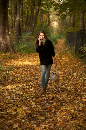 girl talks at smartphone walks in autumn parkの写真素材