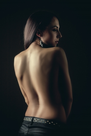brunette woman bared back standing in darkの写真素材