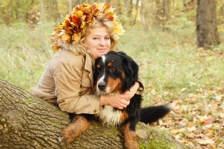 happy smiling mature woman with dog sitting near tree looks at cameraの写真素材