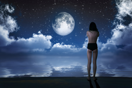 naked girl on sea beach looking at moonの写真素材
