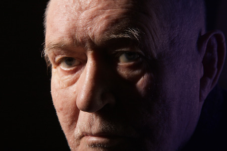serious old man senior in light ray on black backgroundの写真素材