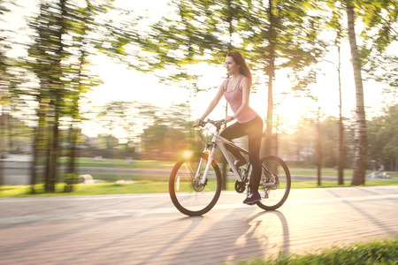 young woman driving on bicycle in evening parkの写真素材
