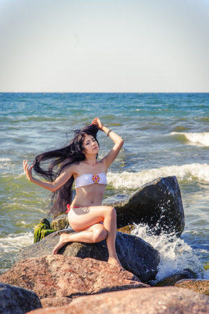 pretty brunette girl plays with hair on stone near seaの写真素材