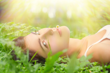 pretty young woman lying in grass under sun raysの写真素材