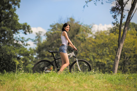 girl walking with bike on mountain grassの写真素材
