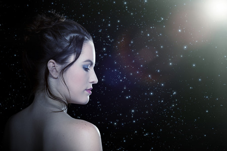 sad pretty girl profile in light rays on stars backgroundの写真素材