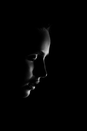 sad young woman profile looking down in dark, monochromeの写真素材
