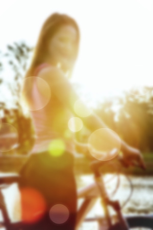 young woman on bicycle in sun light blurred backgroundの写真素材