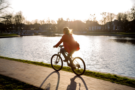 silhouette of girl driving on bike near pond at sunsetの写真素材