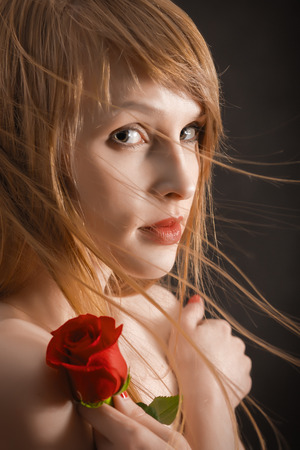 pretty girl with long red hair and red rose on black looking in cameraの写真素材