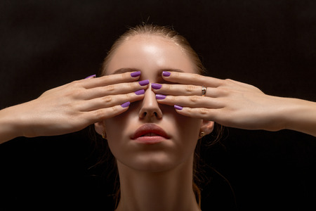 young woman with covered eyes on black backgroundの写真素材