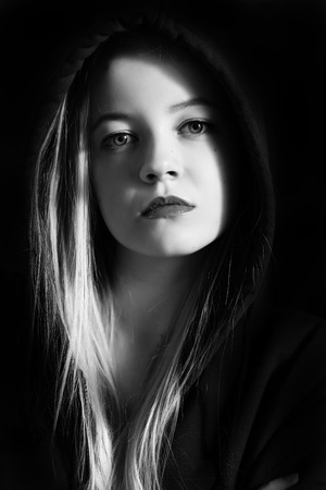 pensive young woman in black hood on black background monochromeの写真素材