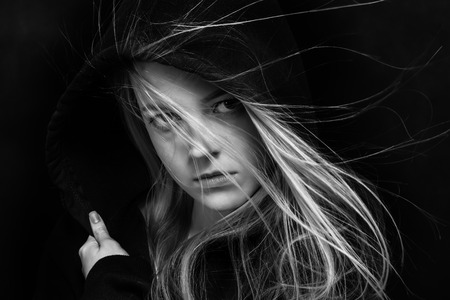 scared girl in black hood in dark monochromeの写真素材