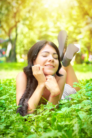 happy girl lying on green grass under sun raysの写真素材