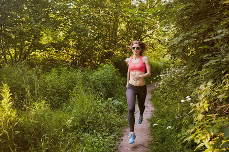 muscular woman running in sunny woodの写真素材