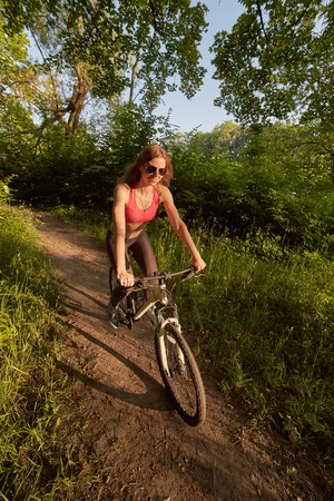 woman moves on bike in wood at sunsetの写真素材