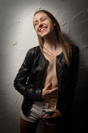 happy blond girl in leather jacket near wallの写真素材