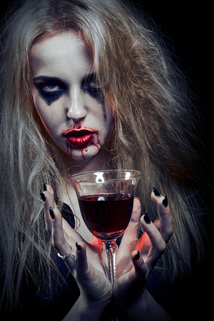blond witch with bloody glass on black background, toned imageの写真素材