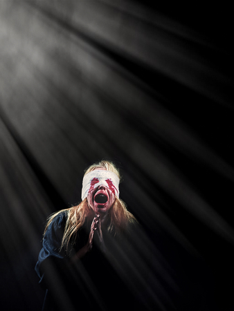 wounded scared bloody girl screaming in light rays on black background with copyspaceの写真素材