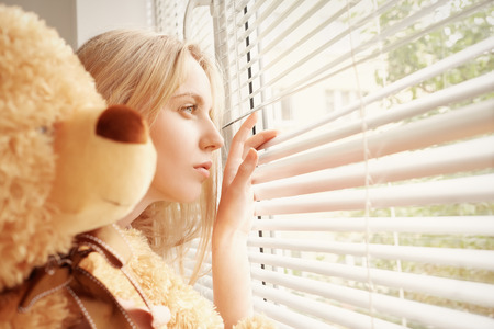 sad girl with teddy bear looking in windowの写真素材